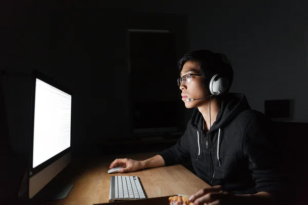 Man met behulp van de computer en het eten van pizza in donkere kantoor — Stockfoto