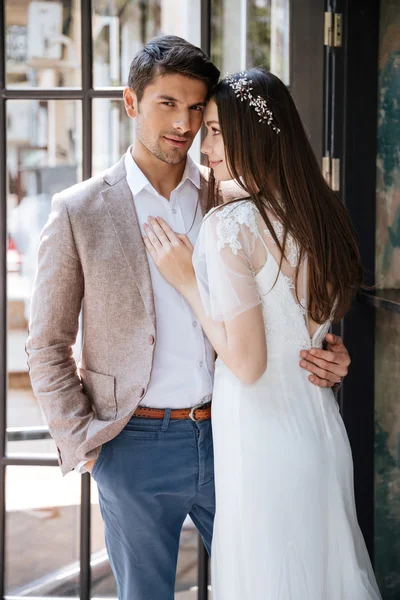 Hermosa joven pareja de boda de pie y abrazando — Foto de Stock