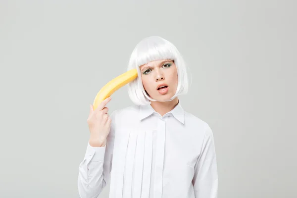 Playful pretty young woman holding banana near her temple — Stock Photo, Image