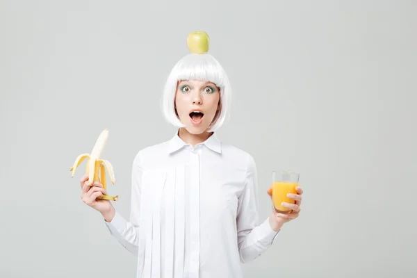 Wondered young woman with apple on her head holding banana — Stock Photo, Image