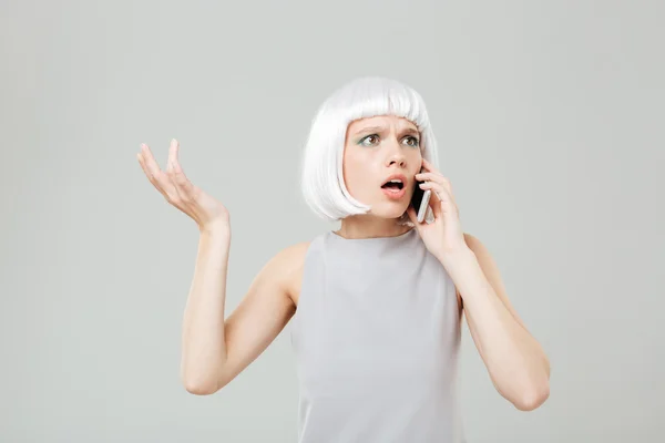 Puzzled worried woman in blonde wig talking on mobile phone