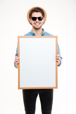 Boş beyaz tahta tutan şapka ve güneş gözlüğü neşeli genç adam