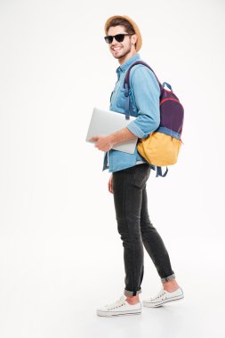 Sırt çantası yürüyüş ve dizüstü bilgisayar tutan neşeli genç adam