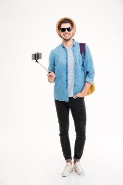 Smiling man with backpack and mobile phone on selfie stick clipart