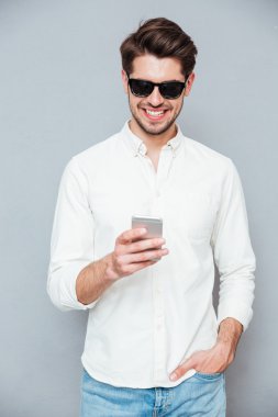 Akıllı telefon kullanarak beyaz gömlek ve güneş gözlüğü gülümseyen genç adam