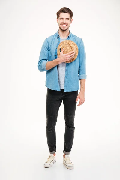 Alegre joven guapo de pie y sosteniendo sombrero — Foto de Stock