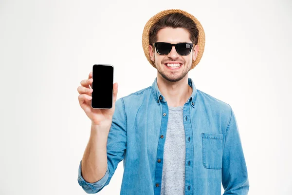 Hombre sonriente con sombrero y gafas de sol sosteniendo teléfono inteligente de pantalla en blanco — Foto de Stock