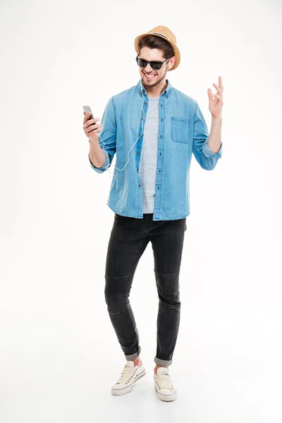 Longitud completa del hombre sonriente escuchando música desde el teléfono inteligente — Foto de Stock