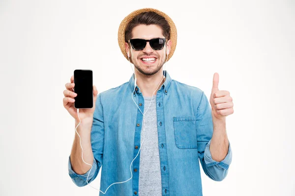 Joven alegre en auriculares que muestran el teléfono celular de pantalla en blanco — Foto de Stock