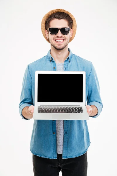 Улыбающийся молодой человек, стоящий и держащий пустой экран ноутбука — стоковое фото