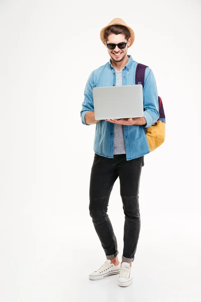Sırt çantası ayakta ve dizüstü bilgisayar kullanarak Mutlu yakışıklı genç adam — Stok fotoğraf