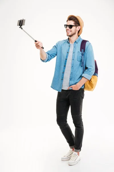 Smiling young man taking photos with smartphone and selfie stick — Stock Photo, Image