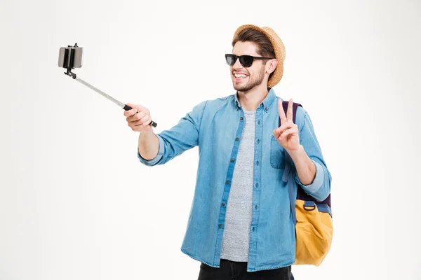 Hombre alegre tomando fotos con el teléfono móvil y palo selfie — Foto de Stock