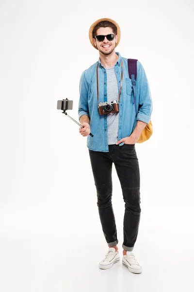 Happy tourist holding backpack, camera and smartphone on selfie stick — Stock Photo, Image