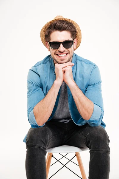 Joven feliz en gafas de sol sentado en la silla y sonriendo — Foto de Stock