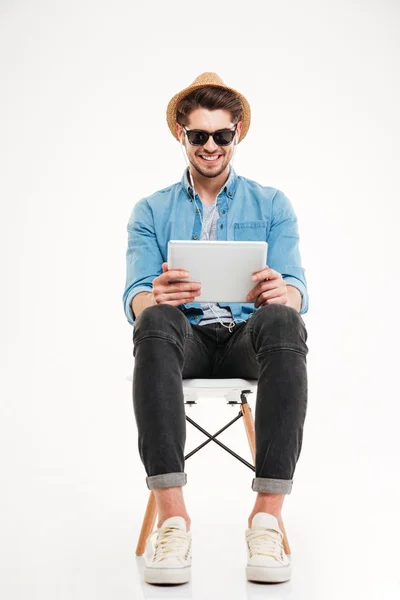 Guapo sonriente macho usando tableta y sentado en la silla — Foto de Stock