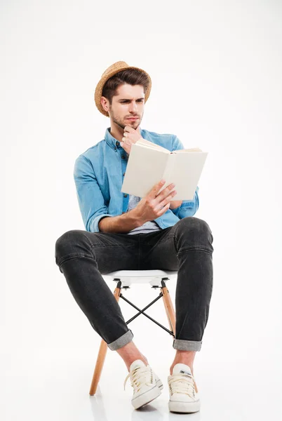 Koncentrerad ung man i hatt sittande och läsa en bok — Stockfoto