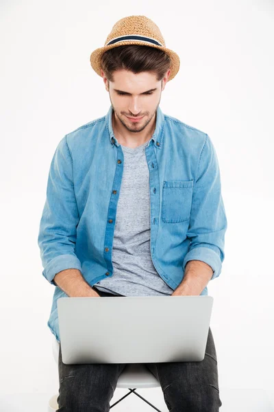Человек в шляпе сидит на стуле и использует ноутбук — стоковое фото
