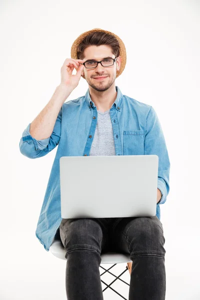 Joven sonriente en gafas y sombrero usando laptop — Foto de Stock