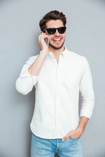 Sonriente joven guapo en gafas de sol hablando por teléfono móvil — Foto de Stock
