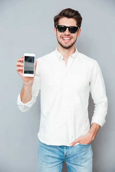 Feliz joven en gafas de sol sosteniendo pantalla en blanco teléfono celular — Foto de Stock