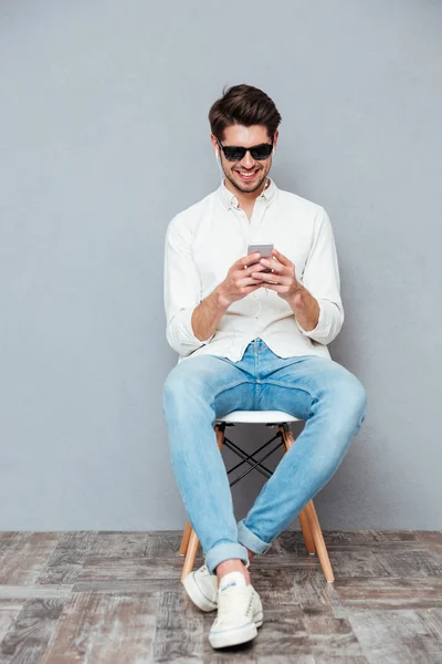 Joven feliz con gafas de sol escuchando música desde un smartphone — Foto de Stock