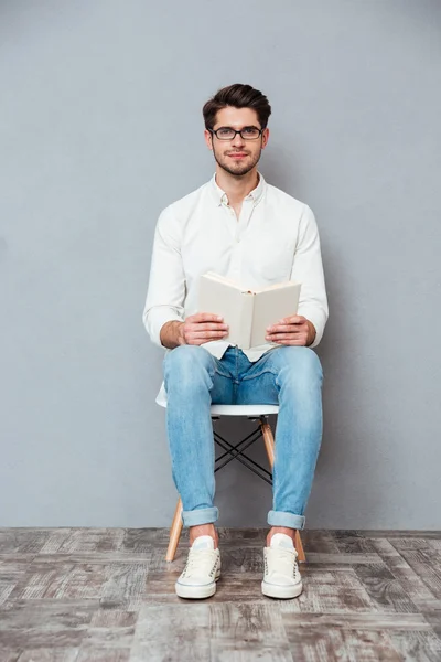 Красивый молодой человек в очках сидит и читает книгу — стоковое фото
