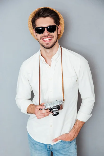 Усміхнений чоловік у капелюсі та сонцезахисних окулярах зі старою старовинною камерою — стокове фото