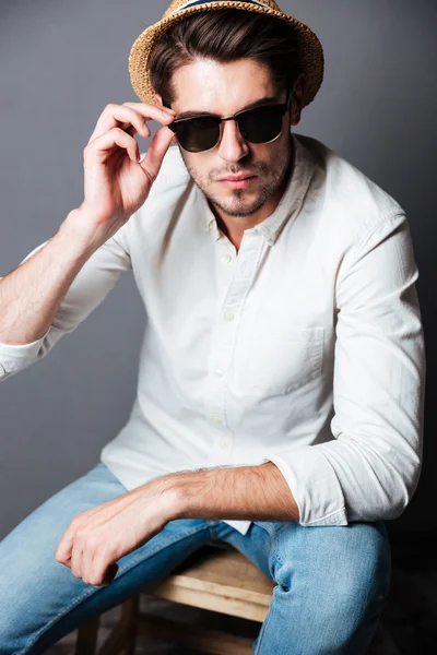 Jeune homme sérieux en chemise blanche, jeans, lunettes de soleil et chapeau — Photo