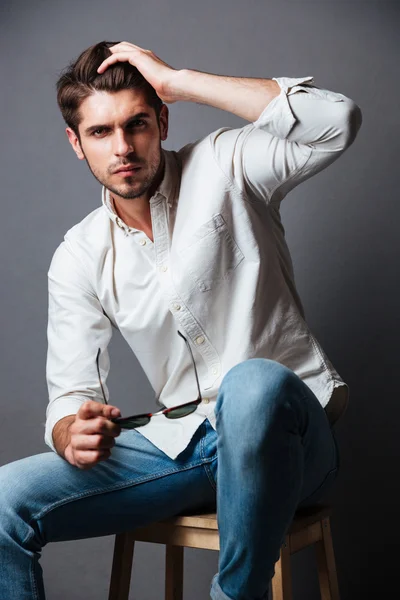 Portrait de mode de jeune homme attrayant assis et portant des lunettes de soleil — Photo