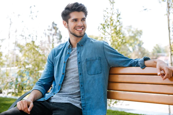 Handsome young man sitting on a bench smiling — Stock Photo, Image