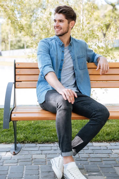 Schöner junger Mann sitzt lächelnd auf einer Bank — Stockfoto