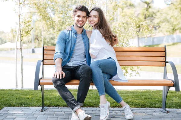 Feliz jovem casal apaixonado sentado em um banco de parque — Fotografia de Stock