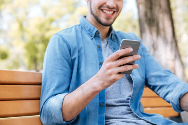 Skadrowana uśmiechnięty mężczyzna z smartphone siedzi na zewnątrz — Zdjęcie stockowe