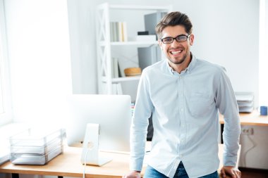 Ofiste ayakta gözlük gülümseyen genç işadamı