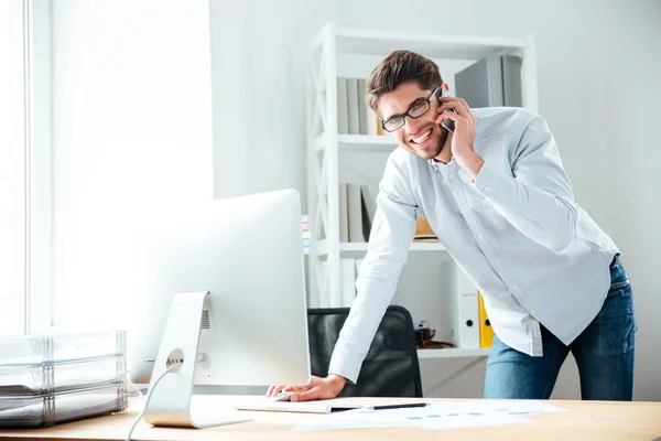 Jovem empresário sorrindo usando computador e falando no celular — Fotografia de Stock