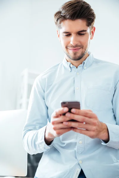 Šťastný atraktivní mladý muž pomocí smartphone v úřadu — Stock fotografie