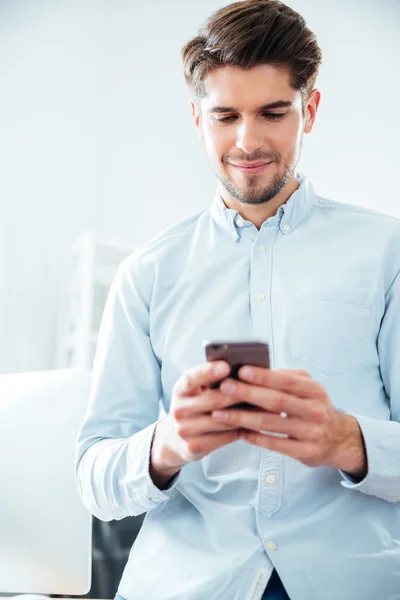 Heureux jeune homme attrayant en utilisant smartphone dans le bureau — Photo