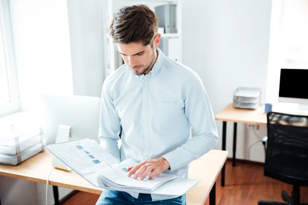 Концентрований молодий чоловік тримає папку з документами в офісі — стокове фото