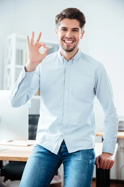 Sorrindo jovem empresário de pé e mostrando sinal ok — Fotografia de Stock