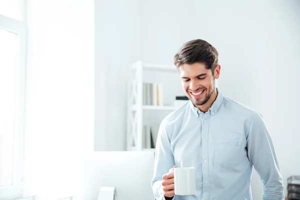 Joven empresario alegre bebiendo café en la oficina — Foto de Stock