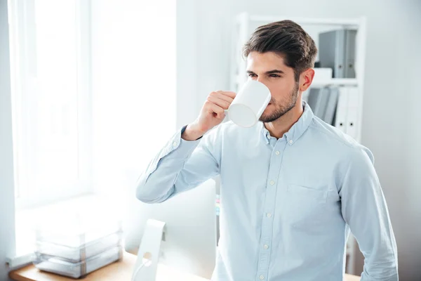 Guapo joven bebiendo café en la oficina — Foto de Stock