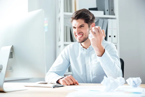 Wütender Geschäftsmann sitzt und zerknüllt Papier an seinem Arbeitsplatz — Stockfoto