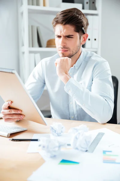 Geconcentreerde jonge zakenman zitten en het lezen van notities in notitieblok — Stockfoto