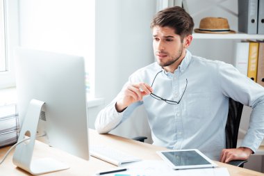 Yakışıklı işadamı gözlük tutan ve bilgisayar monitörü bakıyor