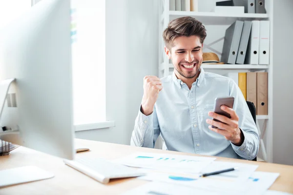 Gelukkig jonge zakenman met behulp van smartphone en het vieren van succes — Stockfoto