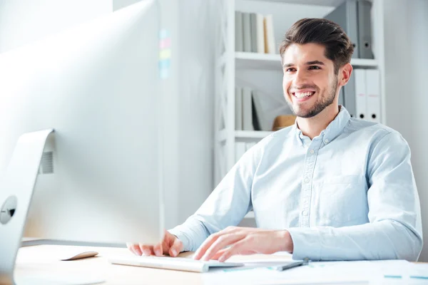 Χαμογελαστός νεαρός επιχειρηματίας χρησιμοποιώντας φορητό υπολογιστή στο γραφείο — Φωτογραφία Αρχείου