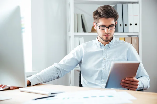 Nachdenklicher Geschäftsmann sitzt und nutzt Tablet-Computer im Büro — Stockfoto