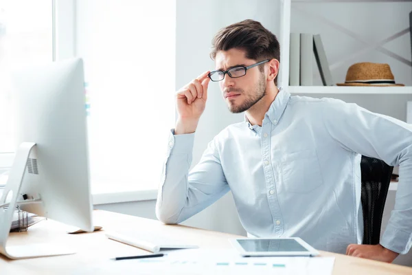 Pensive jonge knappe zakenman in brillen kijken naar computer monitor — Stockfoto