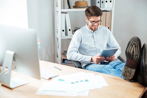 Hombre de negocios sonriente sentado en la mesa y usando tableta —  Fotos de Stock